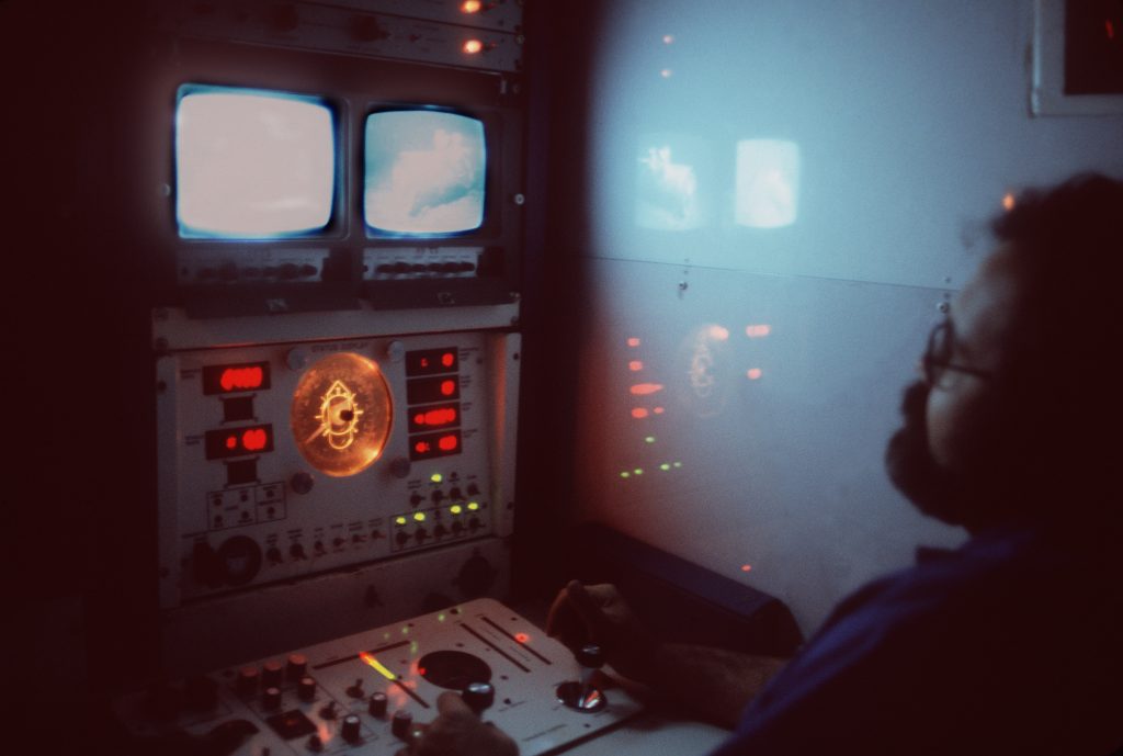 A technician controls the movement of the unmanned submersible Deep Drone from a control panel in the fleet tug USNS NARRAGANSETT (T-ATF 167). The submersible is being used to aid in the search for Korean Air Lines Flight 007. Photo from July 1984 All Hands Magazine.